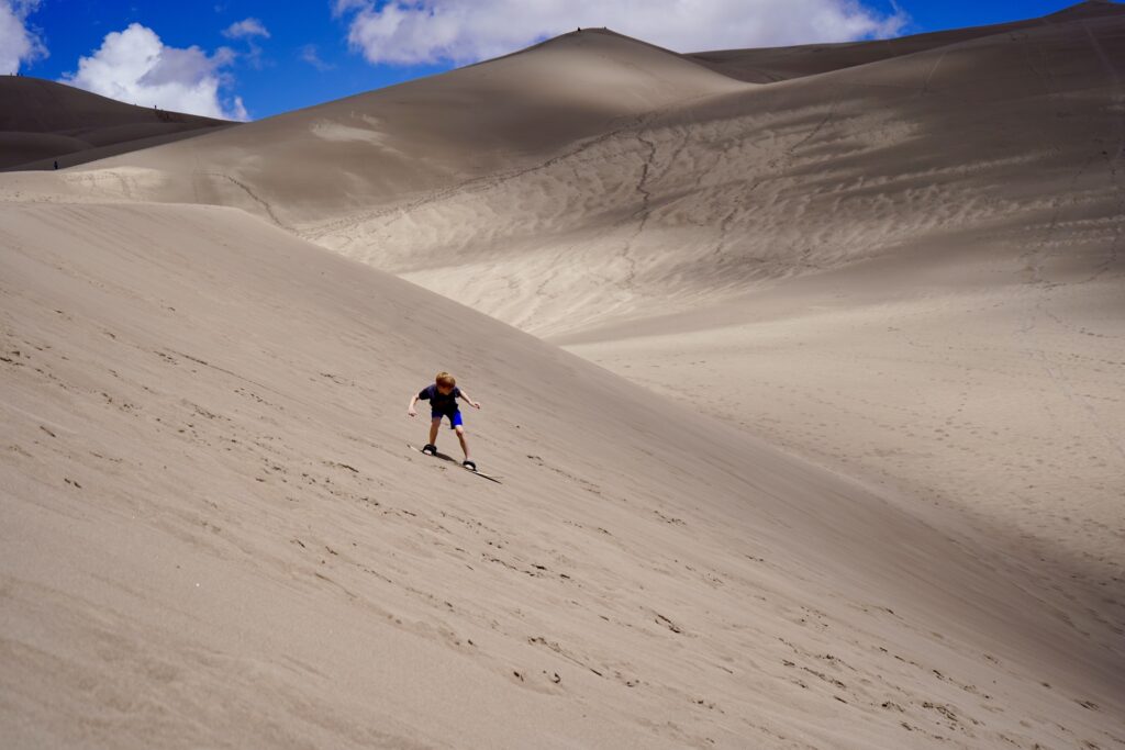 Best things to do in Great Sand Dunes National Park: kid sandboarding down the dune