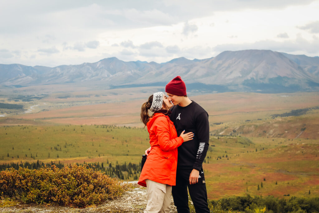 A couple about to kiss in front of a view of fields and mountains.