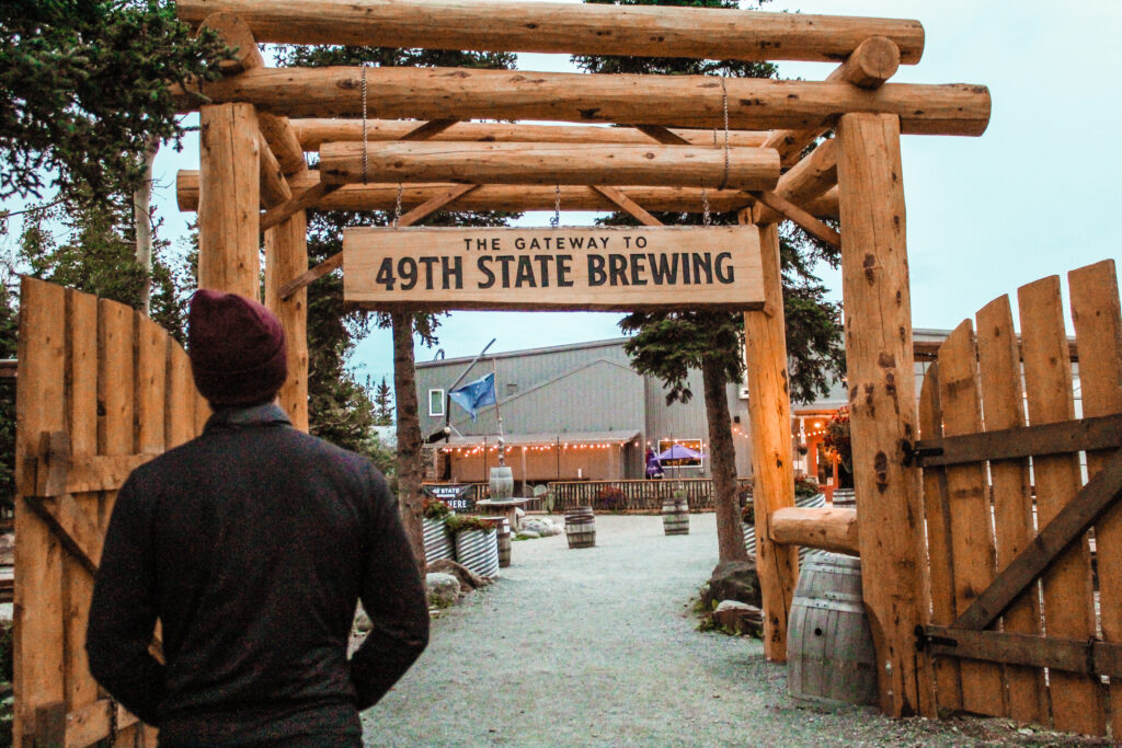 A man walking towards an archway that says 49th State Brewing .