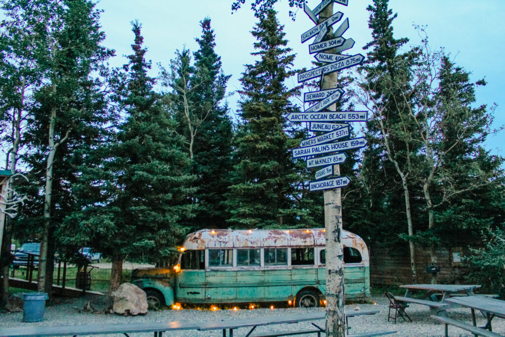 A beaten up teal bus in front of pine trees.