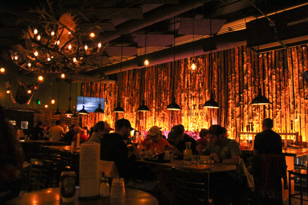 A dimly lit wooden room with antler chandeliers.