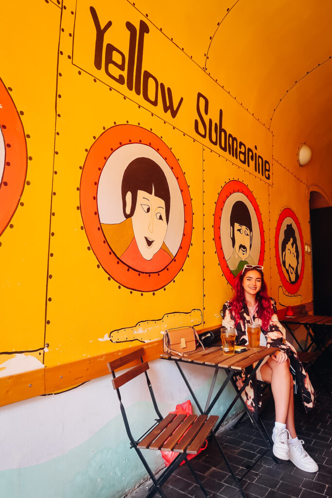 A woman sitting at a table in front of a Yellow Submarine wall.