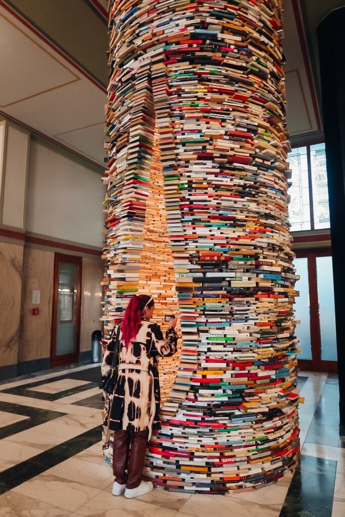 A woman looking into a sliver of a book tower that light comes out of.