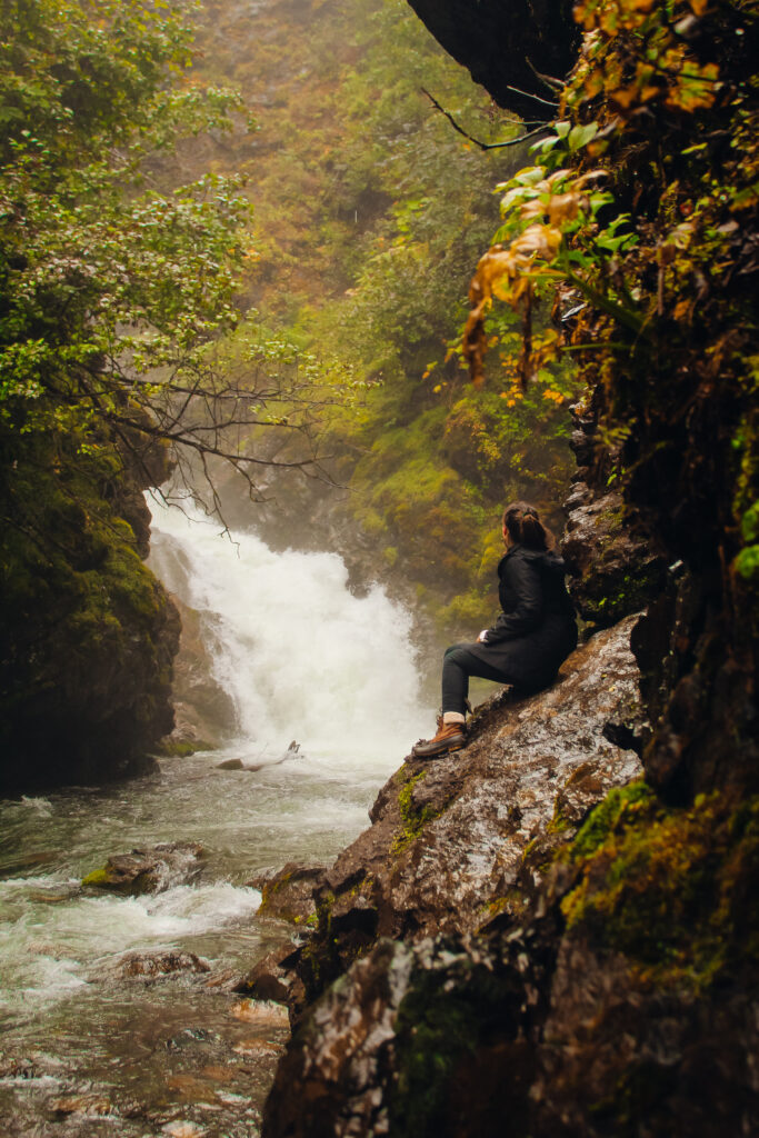 A woman sitting on a rock in front of a waterfall.