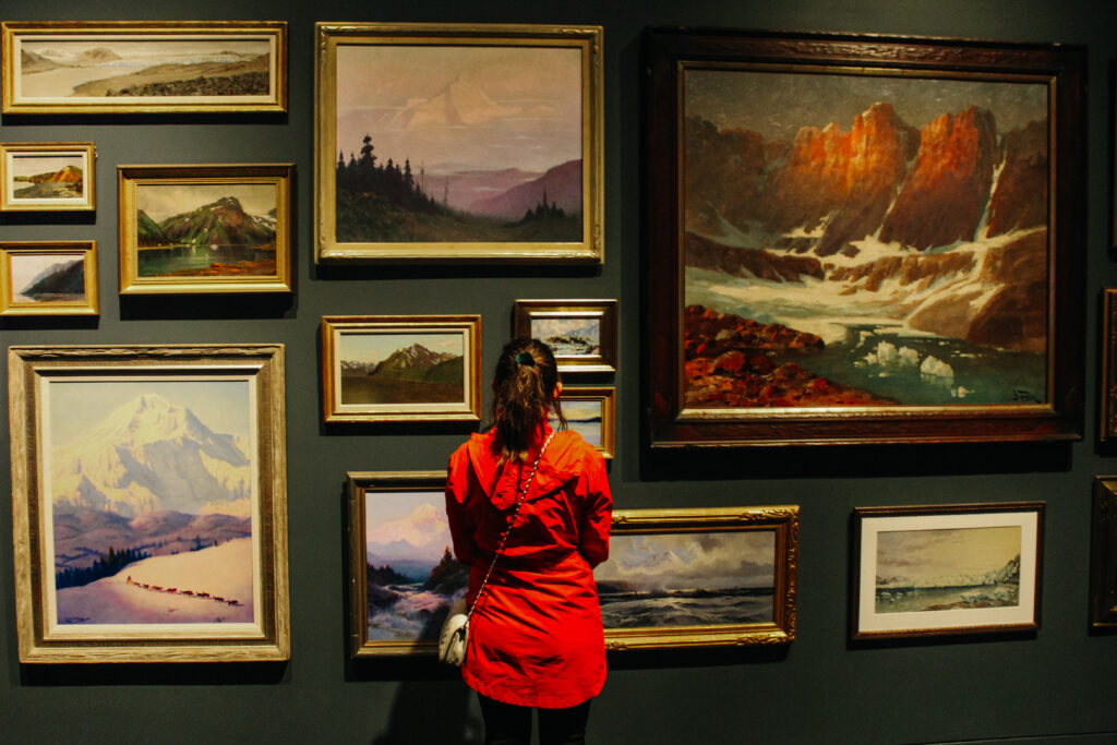 A woman in a red jacket in front of a gallery wall.