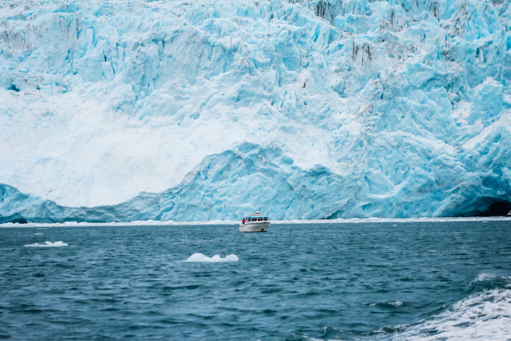 A small boat in front of a large glacier