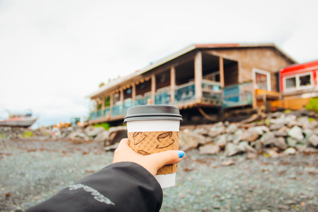 A coffee cup held in front of a wooden resturaunt.