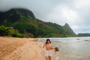 Woman walking along the beach carrying her shoes, mountains in fog in the background.