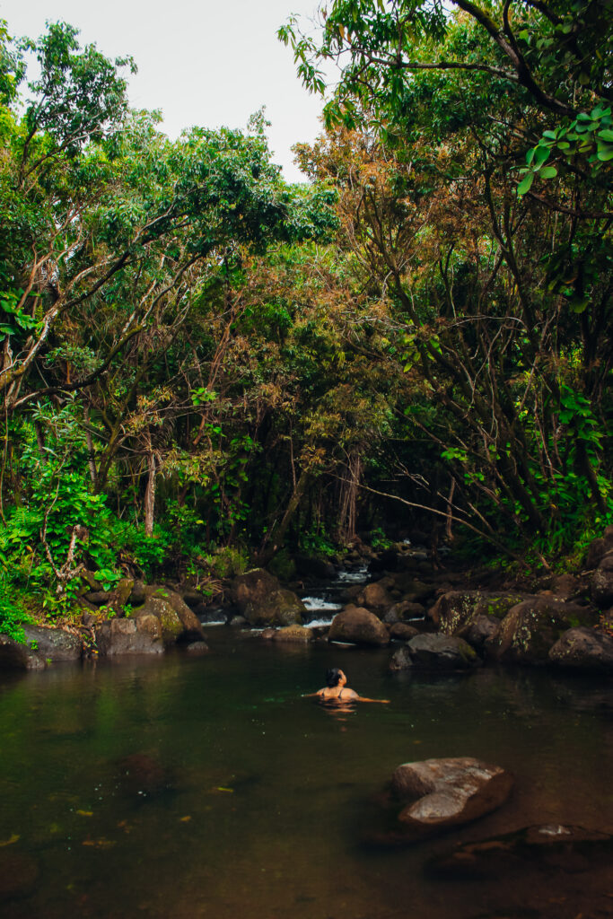 A woman in a small pool at the base of a small waterfall.