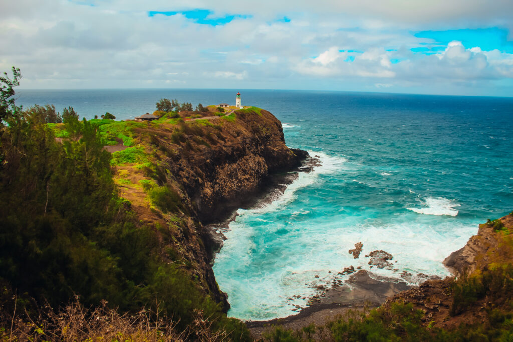 A lighthouse on a cliff with bright blue water surrounding it.