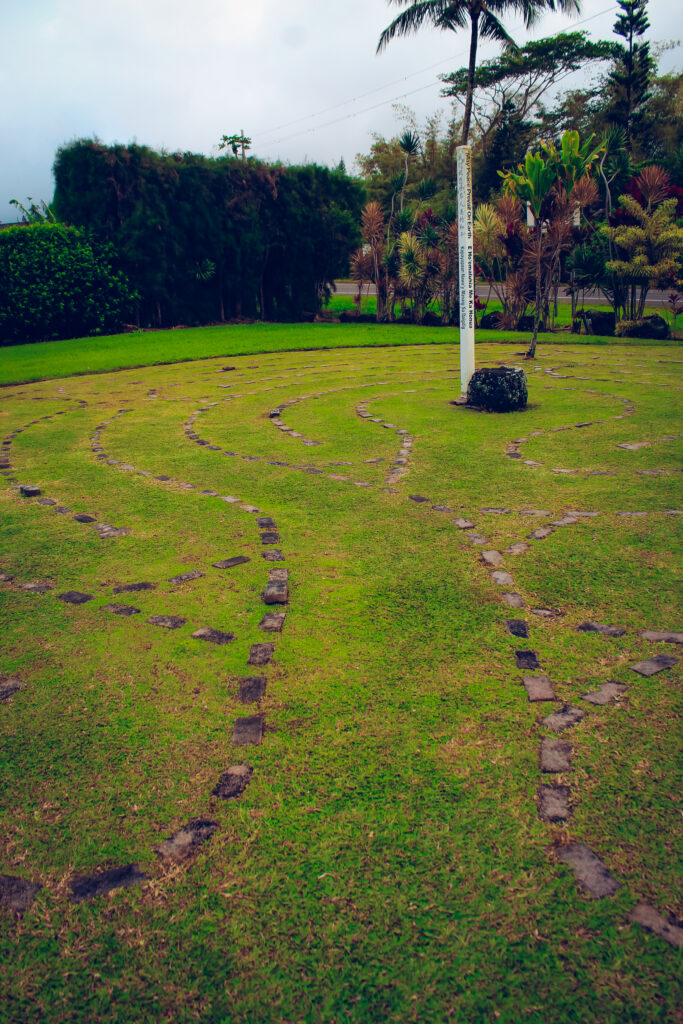 Small Labyrinth made out of stones on green grass. A pole is in the center