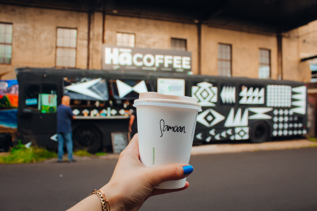 A hand holding a coffee cup in front of a black and white food truck