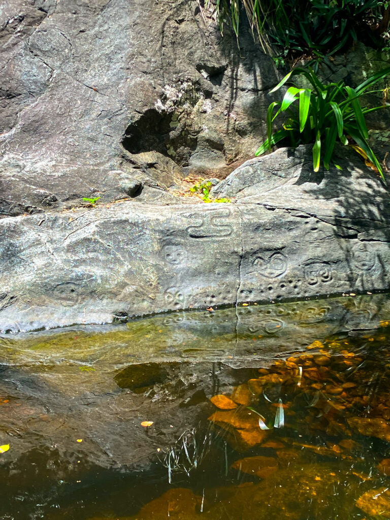 Petroglyphs on stone with water in front of it.