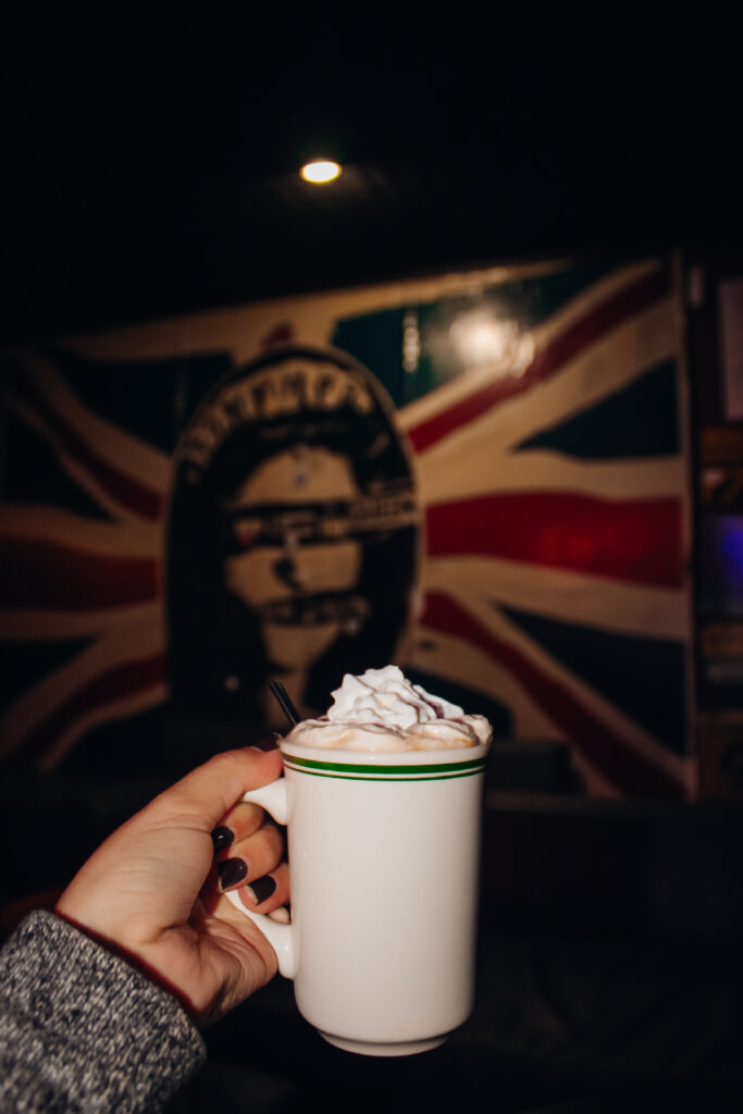 A mug with whipped cream in front of a photo of the british flag.